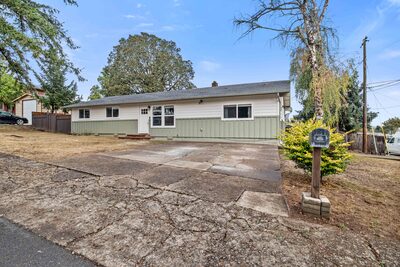 Front exterior with two tone siding, a mature yard tree and a post marking the driveway entrance