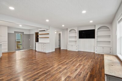 Open living room with white built-in shelving on either side of the television and a clear path to the kitchen