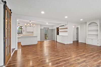 Open concept room with a sliding barn door revealing the kitchen island and pendant chandelier beyond