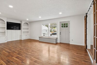 Living room with wood look flooring, white built-in shelving and a front door beside a large window