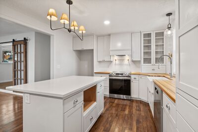 Kitchen island facing a stainless steel range with subway tile backsplash and a farm sink beyond