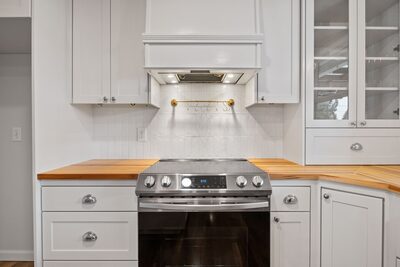 Stainless steel range set between butcher block counters under a custom white hood